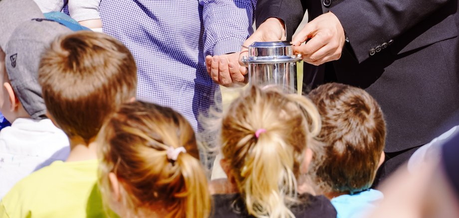 Kinder der Kita Pfiffikus gucken gespannt auf die befüllte Zeitkapsel.
