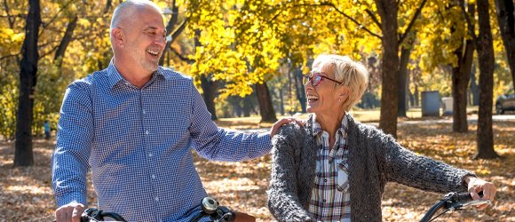 Happy elderly couple riding a bicycle in the park in the autumn