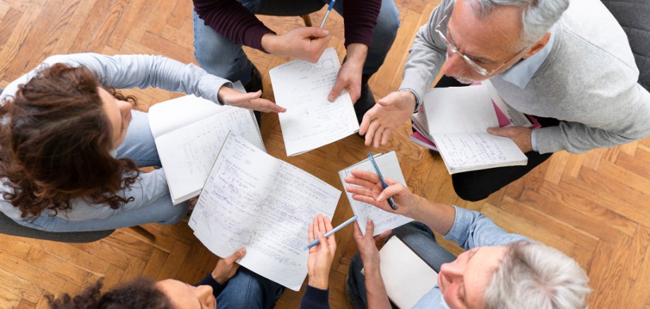 Erwachsene unterschiedlichen Alters sitzen an einem Tisch und diskutieren Themen.