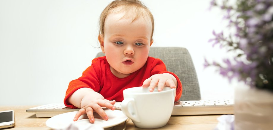 Kleinkind sitzt mit Kaffeetasse am Tisch.