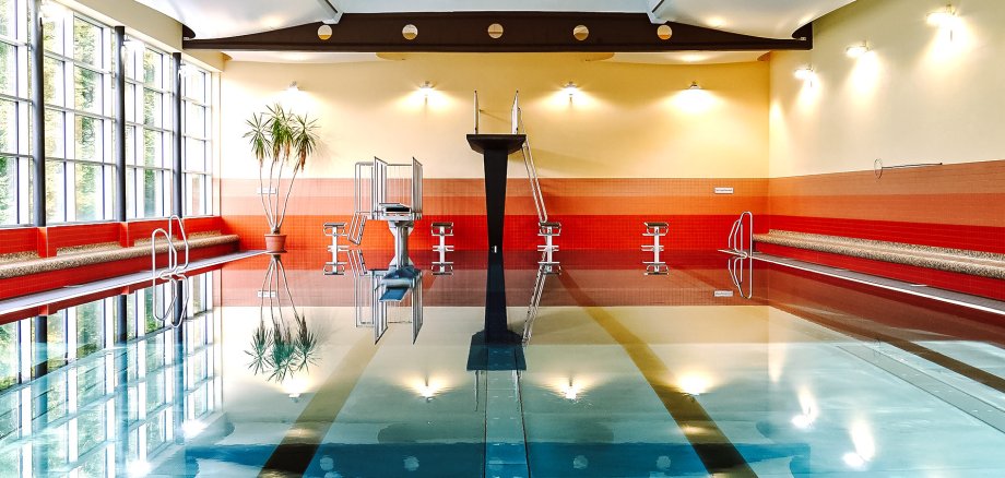 Der 3-Meter-Sprungturm des Hallenbades spiegelt sich im Schwimmbecken.