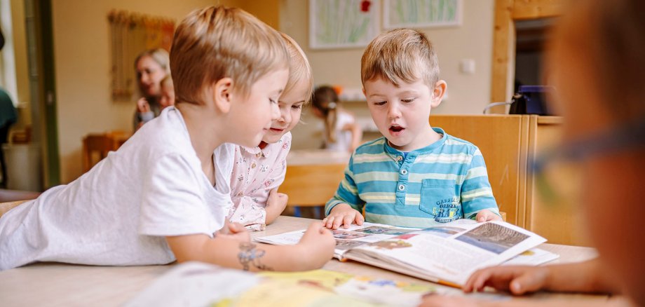Ein Kinder liest begeistert zwei weiteren Kindern etwas aus einem Buch vor.