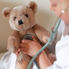 Ein Kind hört seinen Teddybär mit einem Stethoskop ab.